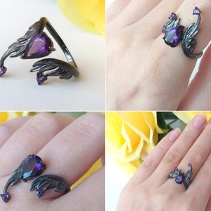 May include: Black ring with a purple gemstone and two wings on either side. The ring is adjustable and can be worn on different fingers.