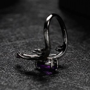 May include: A silver ring with a purple gemstone and the inscription "925" on the band.