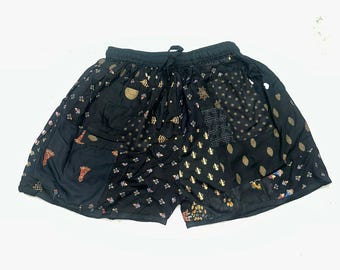 May include: Black shorts with a drawstring waist and a patchwork design. The shorts feature various patterns in gold, red, and white, including floral and geometric motifs. The fabric appears to be lightweight.