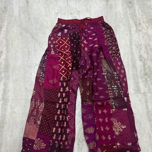 Könnte beinhalten: Weite Patchwork-Hose in Burgunder-, Magenta- und Pflaumentönen. Die Hose besteht aus verschiedenen gemusterten Stoffquadraten, die zu einem einzigartigen, böhmischen Stil zusammengenäht wurden. Der Bund hat einen Kordelzug.