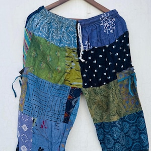 Può includere: Pantaloni patchwork caratterizzati da una varietà di pannelli in tessuto blu, verde e nero con motivi diversi, tra cui stampe floreali, geometriche e astratte. I pantaloni presentano una vita elastica con coulisse bianca e lacci laterali.