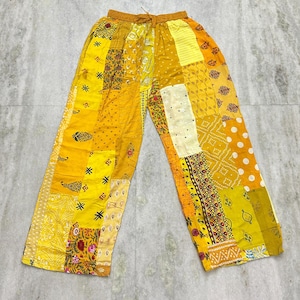 Può includere: Pantaloni gialli patchwork con vita con coulisse. I pantaloni presentano una varietà di tessuti gialli con diversi motivi, tra cui floreali, pois e geometrici. I pantaloni hanno un modello a gamba larga.