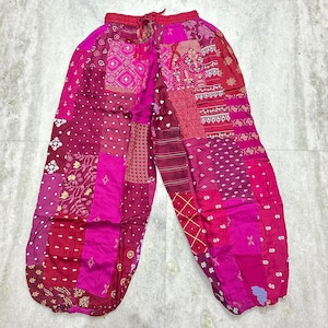May include: Patchwork pants in shades of pink, magenta, and burgundy. The pants feature a drawstring waist and a loose, comfortable fit. The fabric is a mix of patterned and solid patches, creating a unique and bohemian style.