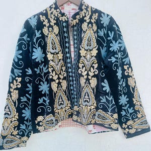 May include: Black velvet jacket with detailed gold, silver, and light blue floral embroidery. The jacket has a mandarin collar and patterned lining. The embroidery forms an ornate design across the front and sleeves.