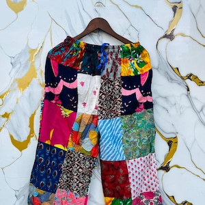 Op de afbeelding: Patchworkbroek met een verscheidenheid aan kleurrijke stoffen vierkanten. De broek heeft een elastische tailleband met een trekkoord. Het patchwork bevat bloemen-, paisley- en geometrische patronen in roze, blauwe, groene en gele tinten.