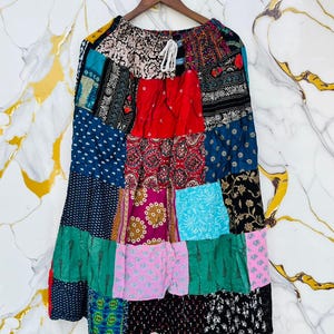 May include: A patchwork skirt with a variety of colorful fabric patterns, including floral, paisley, and geometric designs. The skirt is hanging on a wooden hanger. The skirt has a drawstring waist and a flared silhouette.