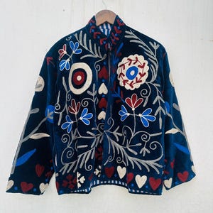 May include: A dark blue velvet jacket with intricate floral embroidery in red, white, and blue. The jacket features a high collar and a full-length zipper. The design includes heart and floral motifs.