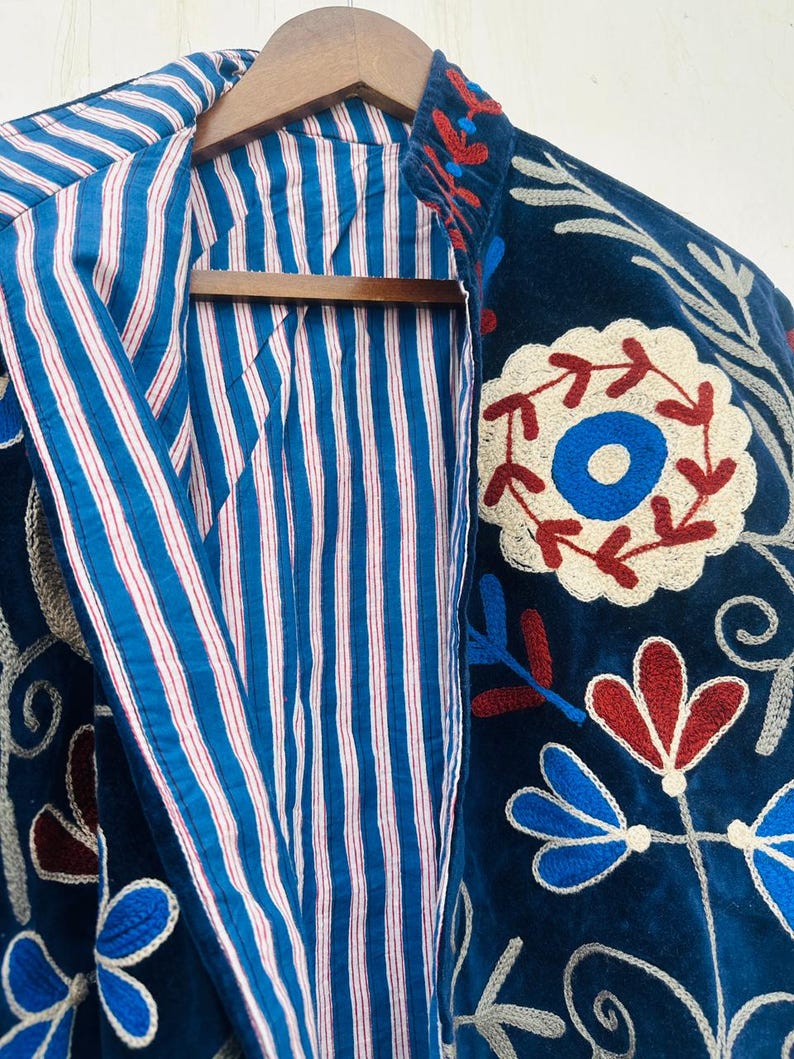 May include: A dark blue embroidered jacket with a striped blue and white lining. The jacket features floral embroidery in red, white, and blue. The jacket is hanging on a wooden hanger.