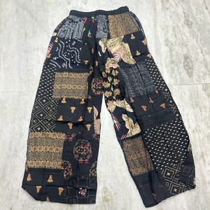 Może przedstawiać: Czarne spodnie patchwork z różnorodnymi wzorami i fakturami. Spodnie prezentują mieszankę geometrycznych, kwiatowych i abstrakcyjnych wzorów w odcieniach czerni, brązu i beżu. Spodnie z szerokimi nogawkami mają elastyczną talię.