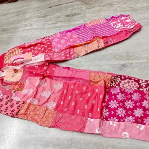 May include: Pink patchwork trousers with a drawstring waist. The trousers display a variety of pink and red patterns, including floral and geometric designs. The fabric appears lightweight and suitable for warm weather.