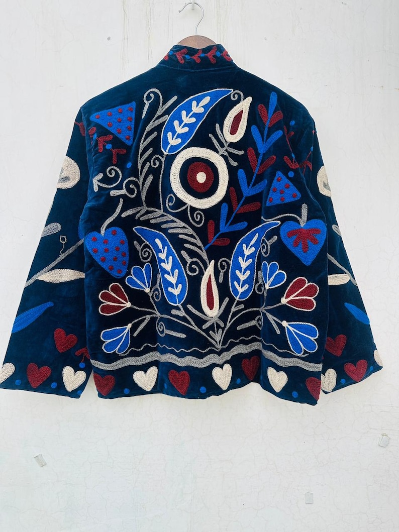 May include: A dark blue jacket with intricate embroidery. The design features red, white, and blue floral and heart motifs. The jacket has long sleeves and a high collar, with the embroidery covering the back and sleeves.