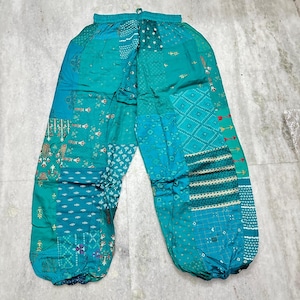 以下が含まれることがあります： ターコイズとティールのパッチワークパンツ。ウエストはゴム入り、足首はギャザー仕様。青と緑の色合いで、幾何学模様と花柄が組み合わされています。生地は薄手で、暖かい季節に適しているようです。