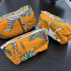 May include: Three orange zippered pouches with a textured surface. Each pouch features a unique animal print design, including zebras and leopards, set against a backdrop of tropical foliage. The pouches are likely for cosmetics or small items.
