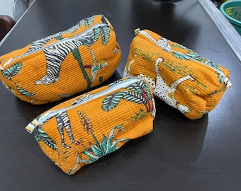 May include: Three orange zippered pouches with a textured surface. Each pouch features a unique animal print design, including zebras and leopards, set against a backdrop of tropical foliage. The pouches are likely for cosmetics or small items.