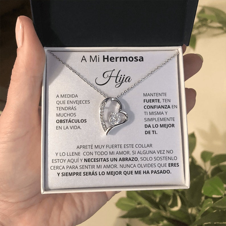 May include: A silver necklace with a heart pendant that says "Hija" and a message in Spanish that reads "A medida que envejeces tendr&aacute;s muchos obst&aacute;culos en la vida. Mantente fuerte, ten confianza en ti misma y simplemente da lo mejor de ti. Apret&eacute; muy fuerte este collar y lo llen&eacute; con todo mi amor. Si alguna vez no estoy aqu&iacute; y necesitas un abrazo, solo sost&eacute;nlo cerca para sentir mi amor. Nunca olvides que eres y siempre ser&aacute;s lo mejor que me ha pasado."