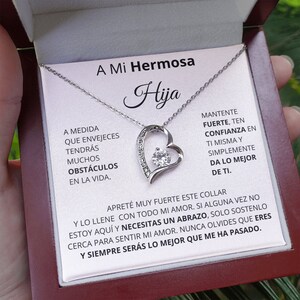May include: A silver necklace with a heart pendant featuring a clear crystal. The necklace comes in a box with a message that reads "A Mi Hermosa Hija" and includes a heartfelt message about strength, confidence, and love.