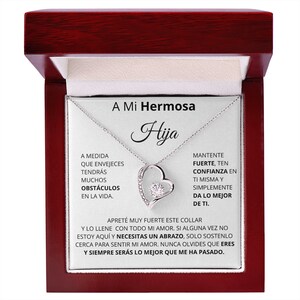 May include: A silver necklace with a heart pendant and a clear crystal stone. The necklace comes in a red wooden box with a message that reads "A Mi Hermosa Hija" and includes a message about strength, confidence, and love.