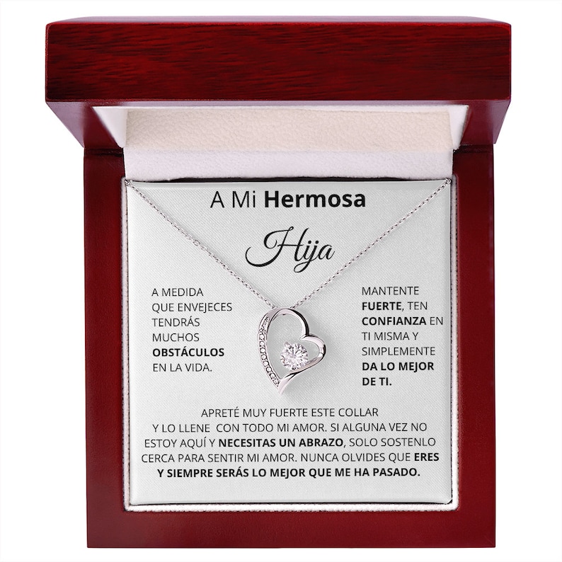 May include: A silver necklace with a heart pendant and a clear crystal stone. The necklace comes in a red wooden box with a message that reads "A Mi Hermosa Hija" and includes a message about strength, confidence, and love.