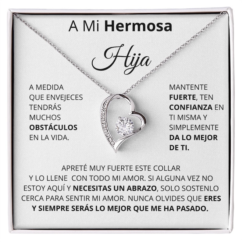 May include: A silver necklace with a heart-shaped pendant featuring a sparkling crystal. The necklace comes in a white box with a message that reads "A Mi Hermosa Hija" and includes a heartfelt message about overcoming obstacles and always being loved.