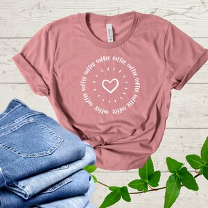 May include: A dusty rose t-shirt with a white circle design featuring the word "coffee" repeated around a white heart.