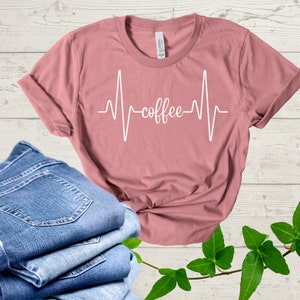 Op de afbeelding: Een roze t-shirt met een witte hartslaggrafiek en het woord "koffie" in de grafiek.