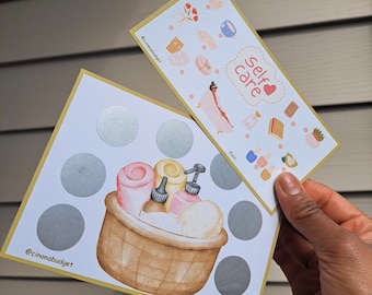 Op de afbeelding: Een kraskaart met een zelfzorgthema met een mand vol badproducten en de tekst "self care" met een hartje. De kaart heeft 8 cirkels met een zilveren kraslaag.