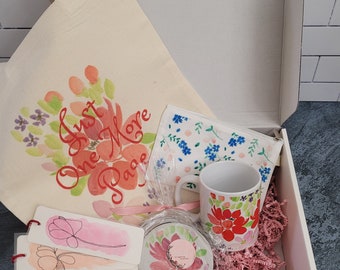 May include: A gift box filled with a white tote bag with the text "Just One More Page" in red, a floral print mug, a floral print coaster, a floral print zippered pouch, and three floral print bookmarks.