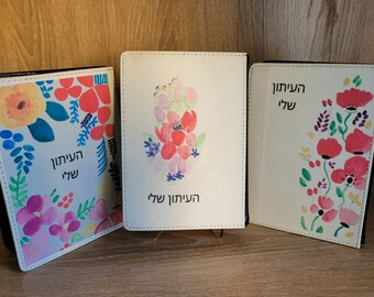 Puede incluir: Tres diarios de cuero blanco con ribetes negros y diseños florales. Los diarios tienen el texto hebreo "El año de mi vida" en la portada.