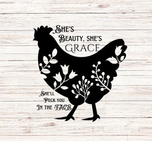 May include: Black silhouette of a chicken with floral designs inside the silhouette. The text "She's Beauty, She's Grace" is above the chicken and the text "She'll Peck You In The Face" is below the chicken.