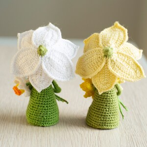 May include: Two crocheted daffodil flower dolls with green bodies and yellow and white flowers.
