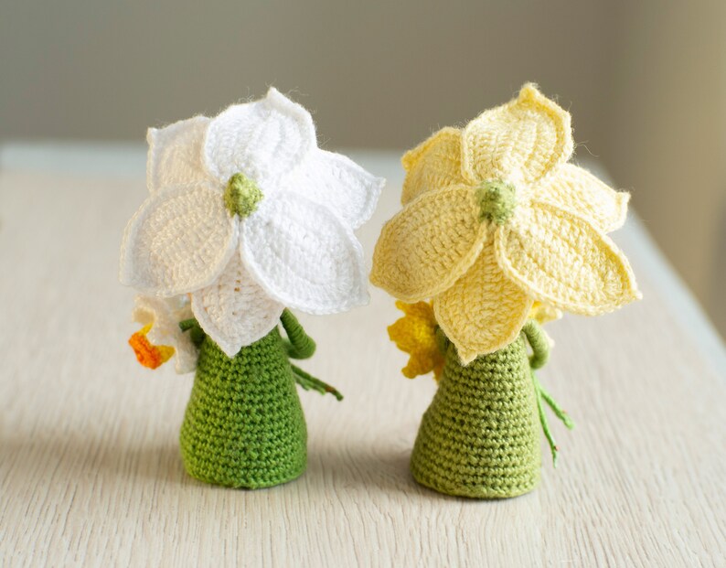 May include: Two crocheted daffodil flower dolls with green bodies and yellow and white flowers.