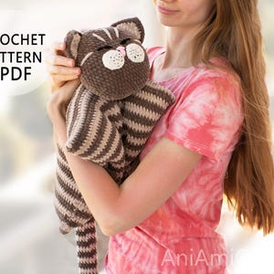 May include: A brown and beige striped crochet cat lovey with a plush head, embroidered eyes, and a pink nose. The text CROCHET PATTERN PDF is visible in the upper left corner. The cat has a soft, textured yarn finish and a long, striped tail.