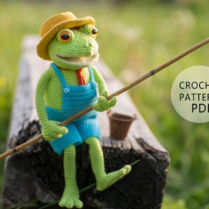 Puede incluir: Una rana de crochet verde con un sombrero amarillo y un mono azul se sienta en un tronco de madera sosteniendo una caña de pescar. La rana tiene una gran sonrisa y ojos naranjas. El texto "CROCHET PATTERN PDF" está en un círculo blanco sobre un fondo verde.