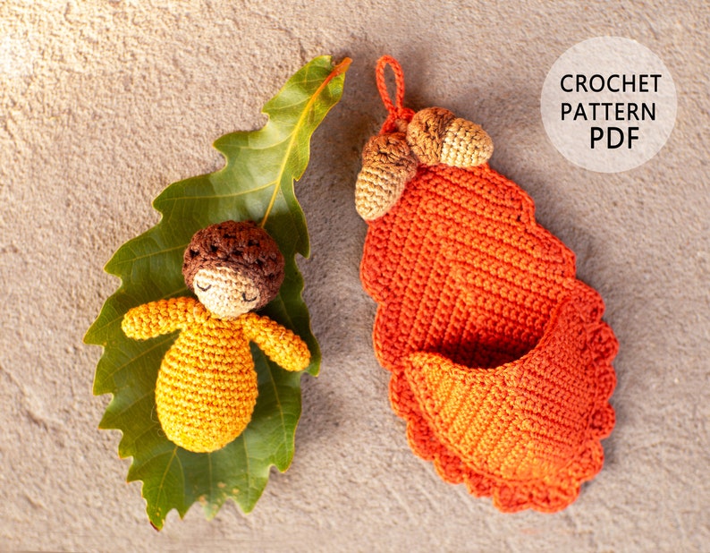 May include: Crochet pattern PDF for a small crocheted doll and a crocheted acorn basket. The doll is laying on a green leaf and the basket is filled with acorns.