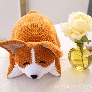 Peut inclure: Un jouet en peluche crochet&eacute; en forme de chien corgi avec du fil orange et blanc, dot&eacute; d'un museau blanc, d'yeux brod&eacute;s noirs et d'un nez noir. Le jouet est positionn&eacute; en position allong&eacute;e avec la t&ecirc;te reposant vers l'avant.
