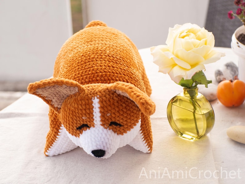 Peut inclure: Un jouet en peluche crochet&eacute; en forme de chien corgi avec du fil orange et blanc, dot&eacute; d'un museau blanc, d'yeux brod&eacute;s noirs et d'un nez noir. Le jouet est positionn&eacute; en position allong&eacute;e avec la t&ecirc;te reposant vers l'avant.