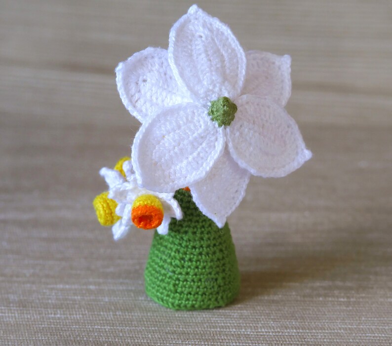 May include: A crocheted flower arrangement in a green vase. The flowers are white with yellow centers.