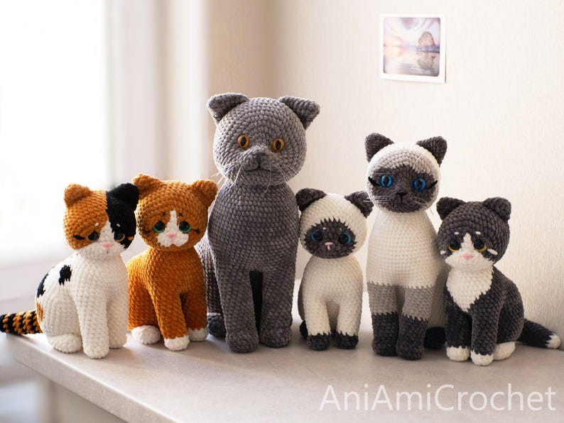 May include: A collection of six crocheted cat plushies in various colors and patterns, including calico, orange, grey, and Siamese styles, all featuring large plastic eyes and stitched details, with the text AniAmiCrochet visible at the bottom.