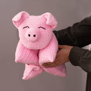 K&ouml;nnte beinhalten: Ein handgeh&auml;keltes Schweinchen-Stofftier aus weichem, hellrosa Garn. Das Kuscheltier hat einen runden Kopf mit gro&szlig;en, h&auml;ngenden Ohren, eine ausgepr&auml;gte Schnauze mit zwei schwarzen Nasenl&ouml;chern und mit schwarzem Faden gestickte, geschlossene Augen.