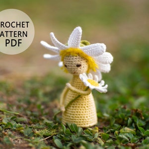 May include: Crochet pattern PDF for a yellow and white crocheted daisy doll holding a white daisy. The doll is standing on green grass.