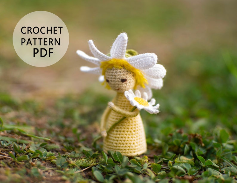 May include: Crochet pattern PDF for a yellow and white crocheted daisy doll holding a white daisy. The doll is standing on green grass.