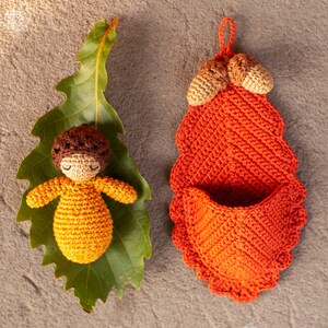 May include: A crocheted acorn doll with brown hair and a yellow dress is lying on a green leaf. A crocheted orange acorn shaped pouch with a brown top is hanging on a brown background.