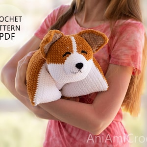 Peut inclure: Un mod&egrave;le de crochet PDF pour un jouet corgi en peluche. Le jouet est fait de fil marron et blanc avec une texture douce, pr&eacute;sentant un visage blanc, des oreilles marron, ainsi qu'un nez et des yeux brod&eacute;s en noir. Texte CROCHET PATTERN PDF et AniAmiCrochet.
