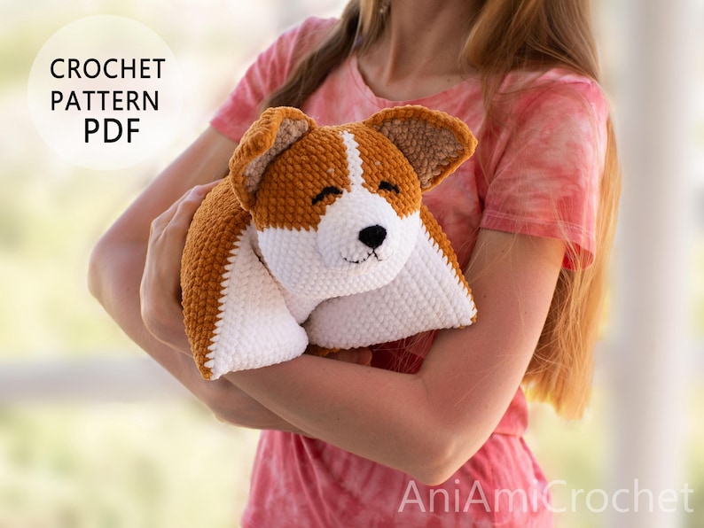 Peut inclure: Un mod&egrave;le de crochet PDF pour un jouet corgi en peluche. Le jouet est fait de fil marron et blanc avec une texture douce, pr&eacute;sentant un visage blanc, des oreilles marron, ainsi qu'un nez et des yeux brod&eacute;s en noir. Texte CROCHET PATTERN PDF et AniAmiCrochet.