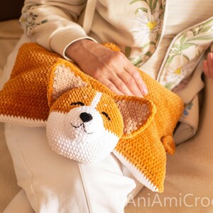 Peut inclure: Un coussin au crochet en peluche, de couleur brun dor&eacute; et blanc, en forme de chien Corgi. Le coussin pr&eacute;sente une t&ecirc;te de Corgi rembourr&eacute;e et d&eacute;taill&eacute;e avec des yeux brod&eacute;s, un nez noir et des oreilles textur&eacute;es sur un corps rectangulaire.