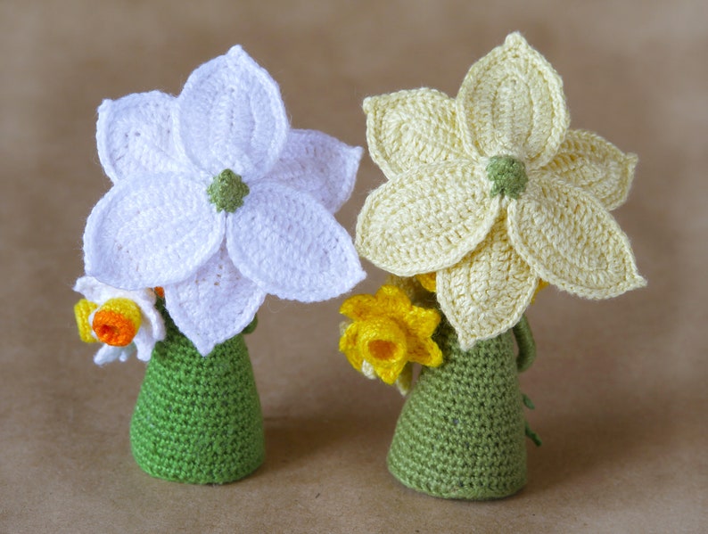 May include: Two crocheted daffodils, one white and one yellow, with green crocheted pots. The daffodils have a 3D effect and are made with a textured stitch.