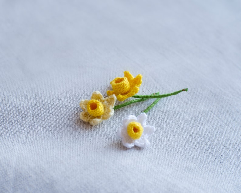 May include: Three crocheted daffodils, one white and two yellow, with green stems.