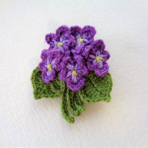 May include: A crocheted purple flower bouquet with green leaves. The flowers have yellow centers.