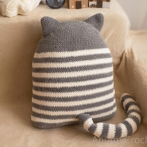 May include: Gray and white striped crocheted cat pillow with a long tail. The pillow has a gray crocheted head with cat ears.