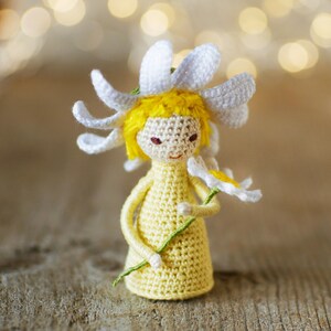 May include: A crocheted doll with yellow hair and a white daisy flower hat holding a green stem with a white daisy flower.